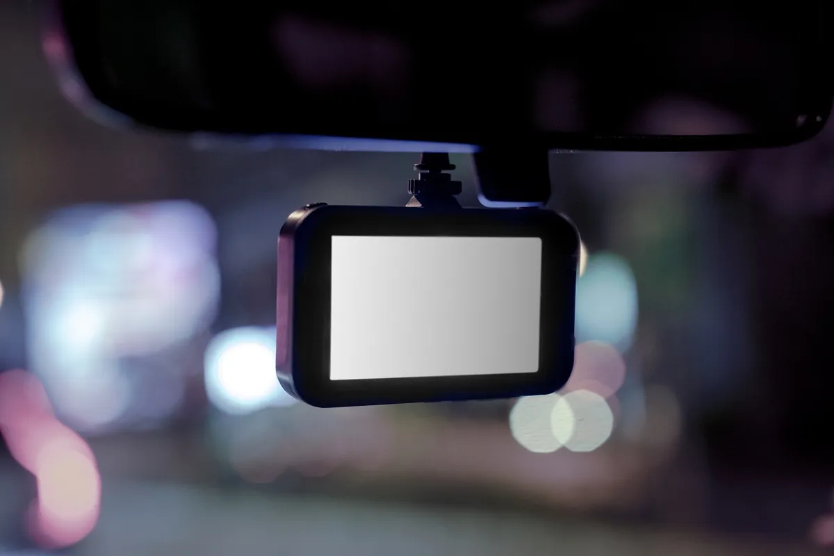 Eine Dashcam an der Windschutzscheibe eines Autos, dahinter verschwommene Lichter der Stadt