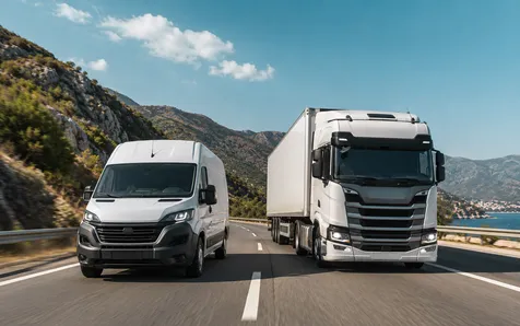 O dubă albă și un camion circulând pe o șosea de coastă