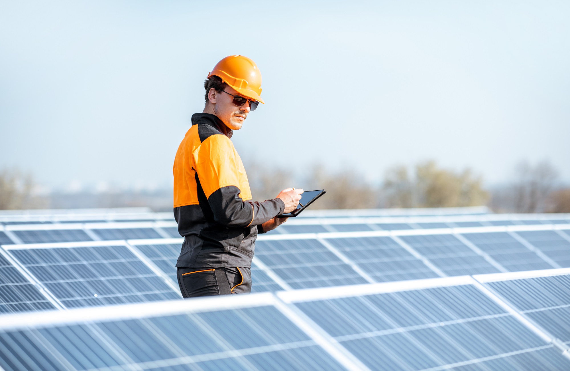 Engineer in protective workwear carrying out service of solar panels with digital tablet on a photovoltaic rooftop plant. Concept of maintenance and setup of solar power station