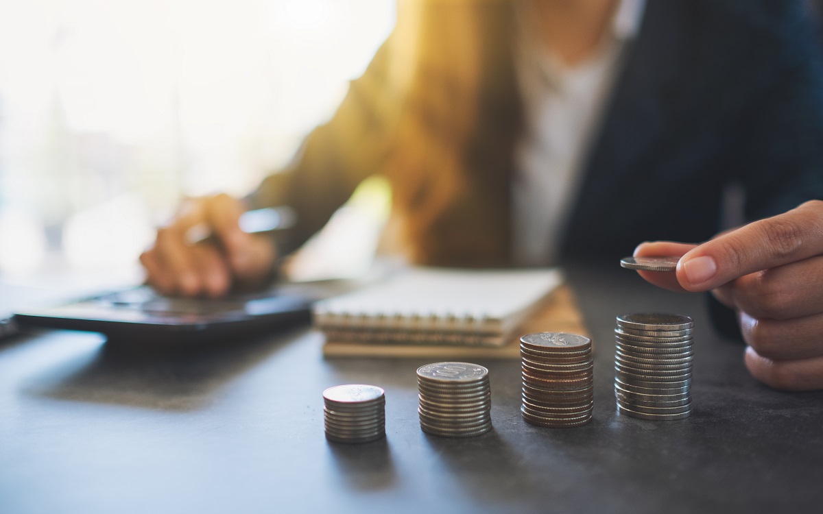 Businesswoman holding and stacking coins while calculating money on the table