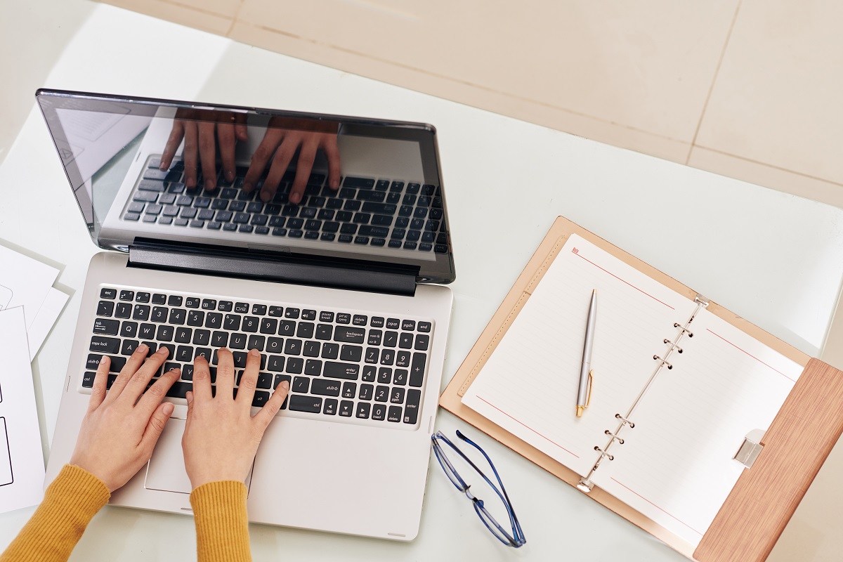 Hands of female back end developer working on laptop with her opened planner near by